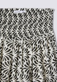 Gonna smockata bianca e nera con un motivo floreale e disegni a forma di foglia. Materiale leggero con una vita arricciata. Etichetta del marchio visibile.