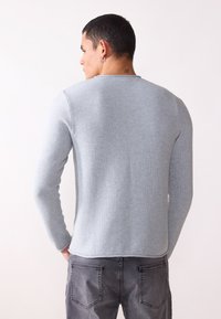Pull en tricot gris clair à manches longues, col rond et motif texturé. Associé à un Jean gris avec poches arrière.