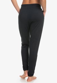 Zwarte, lichte joggingsbroek van zacht materiaal, met een rekbare tailleband en boorden bij de enkels, ontworpen voor comfort en bewegingsvrijheid.