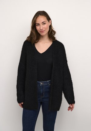 Cardigan nero con texture, aperto sul davanti e maniche lunghe, indossato sopra un top nero con scollo a V, abbinato a jeans blu.