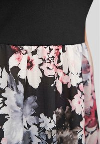 Un haut noir avec une jupe à motifs floraux mélangeant des fleurs roses, blanches et grises sur un fond noir ; tissu léger et doux avec une taille élastique.