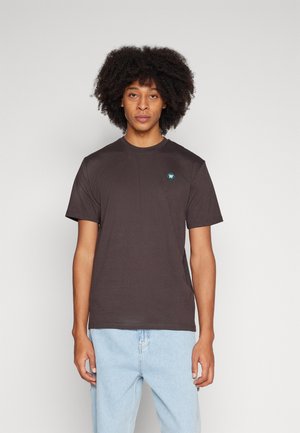 Brown crew neck t-shirt made of cotton, featuring a small green logo on the left chest, short sleeves, and a relaxed fit.