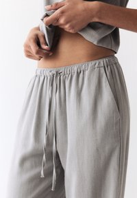 Jogging gris clair, léger, avec une taille élastique, un cordon de serrage et des poches latérales. Texture douce avec un léger éclat.