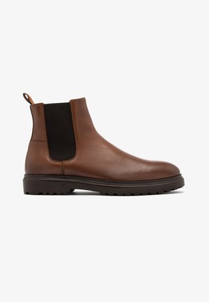 Brązowe skórzane botki Chelsea z elastycznymi panelami bocznymi, teksturowaną gumową podeszwą i płaskim obcasem. Wyposażone w pętelkę z kolorowym akcentem z tyłu.