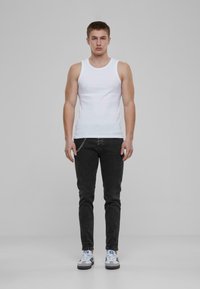 Camiseta sin mangas blanca, de material de algodón, diseño ajustado. Jeans de mezclilla negros con detalle de cadena. Calzado casual con acentos grises y azules.