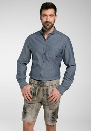 Herrenhemd in Blau mit Knopfleiste und Brusttasche, kombiniert mit grauen Leder-Shorts mit floralem Stickmuster und einer dekorativen Gürtelschnalle.