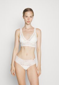 Bralette en dentelle blanche et culottes assorties. La bralette présente des bretelles en dentelle larges, un col en V et un motif floral délicat. Texture douce et transparente tout au long.