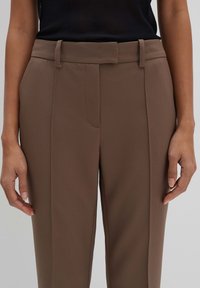 Pantaloni marroni su misura con una texture liscia, vita aderente con cintura e dettagli piesse frontali.