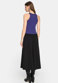 Fioletowy dopasowany top na ramiączkach zestawiony z luźną czarną spódnicą maxi. Spódnica posiada elastyczny pasek w talii i sięga do połowy łydki. Czarne kozaki do kolan doskonale uzupełniają ten zestaw.