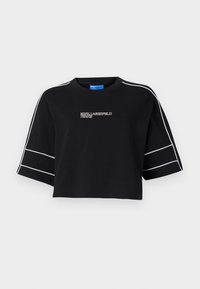 Melna īsā T-kreklā ar īsām, platām piedurknēm. Uz piedurknēm ir baltas svītras, un tajā ir teksts "Karl Lagerfeld Jeans" baltajā krāsā. Izgatavots no kokvilnas materiāla.
