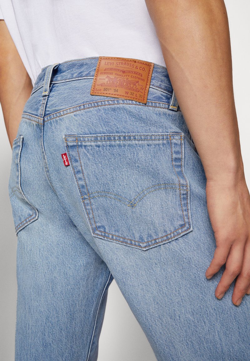 Helle blaue Jeans mit geradem Schnitt, ausgestattet mit einem Lederlogo-Patch und einem roten Tab, die Rückentaschennaht in einem klassischen Bogen-Design.