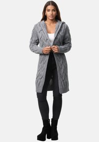 Cardigan lungo grigio a maglia con cappuccio, con polsini a costine e apertura frontale, abbinato a pantaloni neri aderenti e stivali con tacco alto.