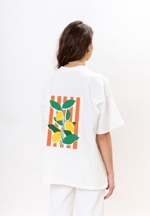 Witte oversized t-shirt met een citroen- en bladontwerp op een gestreepte oranje achtergrond. Ronde hals, korte mouwen, gladde katoenen textuur.