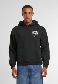Zwarte hoodie met een voorste kangoeroezak en witte "Baby Don't Cry" tekst graphic op de linkerborst. Zachte stof, relaxed fit.