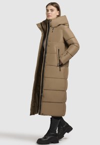 Dlhý béžový prešívaný kabát s vysokým golierom, plným zipsom a bočnými vreckami. Obsahuje prešívanú textúru a elegantný, štíhly dizajn.