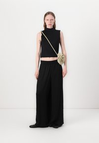 Black sleeveless crop top with high neck, paired with loose black wide-leg pants and a light green bag featuring a gathered design.