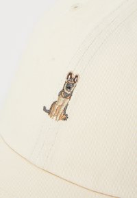 Baseball cap in cream fabric with a textured surface; features an embroidered German Shepherd motif in brown and black on the front.