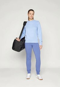 Gaiši zils sporta krekls ar gariem piedurknēm, apvienots ar ziliem joggeriem. Melna sporta soma ar plecu siksnu. Baltas sporta kurpes.