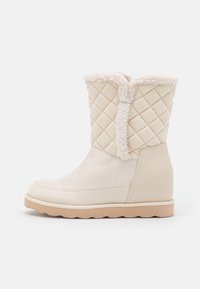 Stivale invernale beige a metà polpaccio con parte superiore trapuntata, bordo in finta pelliccia, tacco texturizzato e suola in gomma marrone chiaro.