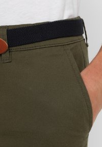 Olivgröna bomullsbyxor med ett marinblått vävt bälte och bruna läderdetaljer, med sidoficka och slät textur.