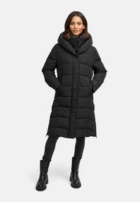 Zwarte gewatteerde jas met een lange, doorgestikte uitstraling, oversized capuchon en zijzakken. Gecombineerd met zwarte jeans en chunky zwarte laarzen.
