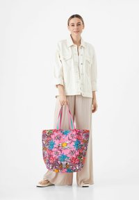 Grote draagtas met een levendig roze bloemenontwerp, voorzien van groene en blauwe accenten en meerkleurige banden. Gemaakt van duurzaam materiaal.