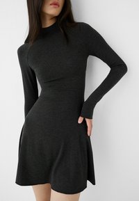 Mörkgrå långärmad klänning med hög krage, figurnära midja och utsvängd kjol. Mjuk textur med en slät yta och sidofickor.