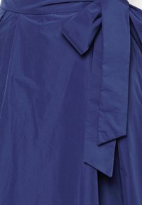 Tummansininen puuvillakangas, jossa on sivusolje, sileä pinta ja jyrkät laskokset hemman reunassa.