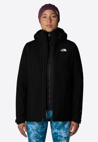 Juodas atsparus vandeniui džemperis su užtrauktuku priekyje, reguliuojama kapuce ir The North Face logotipu. Suderinta su raštuotomis mėlynomis legginsomis.