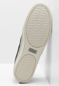 Svart sneaker med gummisula, texturerad botten med fiskbensmönster och en silverfärgad "POLO"-logotyp på sidan.