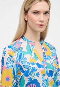 Bluse mit floralem Muster aus leichtem Stoff, die lebendige Blau-, Pink-, Gelb- und Grüntöne zeigt. Sie verfügt über einen Mandarin-Kragen und einen einzelnen Knopfverschluss.