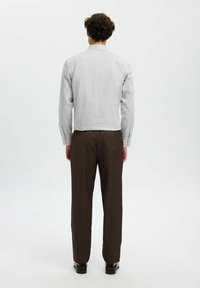 Gestreepte overhemden in lichtgrijs en wit, gecombineerd met een bruine broek. Het overhemd heeft een puntkraag en lange mouwen.