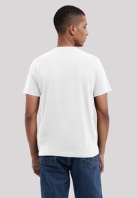 White cotton t-shirt with a crew neck, short sleeves, and a relaxed fit, worn by a person turned slightly to the left.