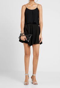 Haut plissé noir avec des bretelles spaghetti, associé à une jupe noire évasée. Les accessoires comprennent une pochette noire en perles et des sandales à talons argentées.