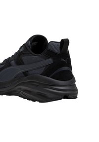 Scarpa atletica nera con una combinazione di materiali in rete e suede, forma arrotondata, dettagli texturizzati e suola ammortizzata.