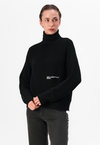 Pulover cu guler înalt negru, prevăzut cu mâneci lungi și o croială lejeră. Detaliu notabil: logo-ul "KARL LAGERFELD JEANS" în alb pe partea din față.