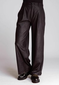 Black high-waist wide-leg leather pants with front pleats, paired with chunky black loafers featuring gold chain detail.