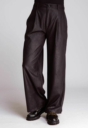 Schwarze, hoch geschnittene, weit geschnittene Lederhosen mit vorderen Falten, kombiniert mit klobigen schwarzen Slippern, die über eine goldene Kettendetail verfügen.