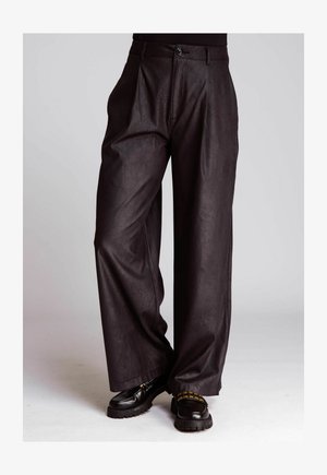 Schwarze, hoch geschnittene, weit geschnittene Lederhosen mit vorderen Falten, kombiniert mit klobigen schwarzen Slippern, die über eine goldene Kettendetail verfügen.