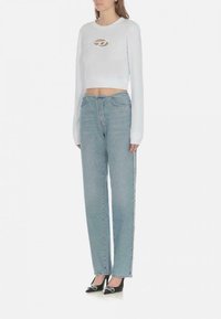 Felpa bianca corta con maniche lunghe e dettagli del logo, abbinata a jeans a vita alta dritti di colore blu chiaro e tacchi alti neri.