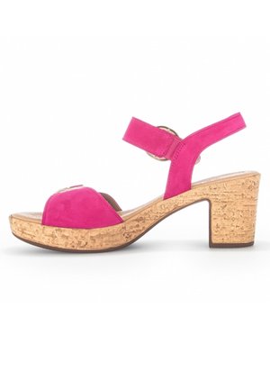 Różowe zamszowe sandały na wysokim obcasie z korkową platformą. Model ma zaokrąglony nosek i pasek wokół kostki zabezpieczony okrągłą ozdobą.