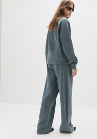 Prevelik teal dukserica i usklađene široke hlače, napravljene od mekog materijala sa suptilnom teksturom, prikazane sa stražnje strane.