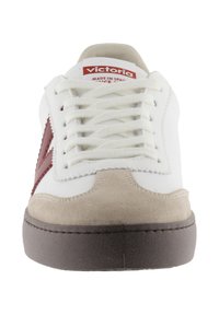 Sneaker bianca con accento rosso sul lato, con puntale in camoscio e lacci. Suola in gomma e marchio "Victoria" sulla linguetta.