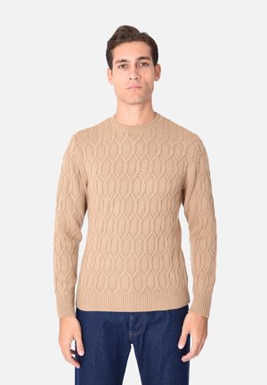 Maglione lavorato a maglia beige con motivo a diamante testurizzato, scollatura rotonda e polsini a coste, abbinato a jeans blu scuro.