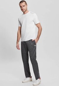 Weißes T-Shirt mit kurzen Ärmeln kombiniert mit schwarzen, gemusterten Hosen mit Reißverschluss am Knöchel und weißen Sneakers mit roten Akzenten.