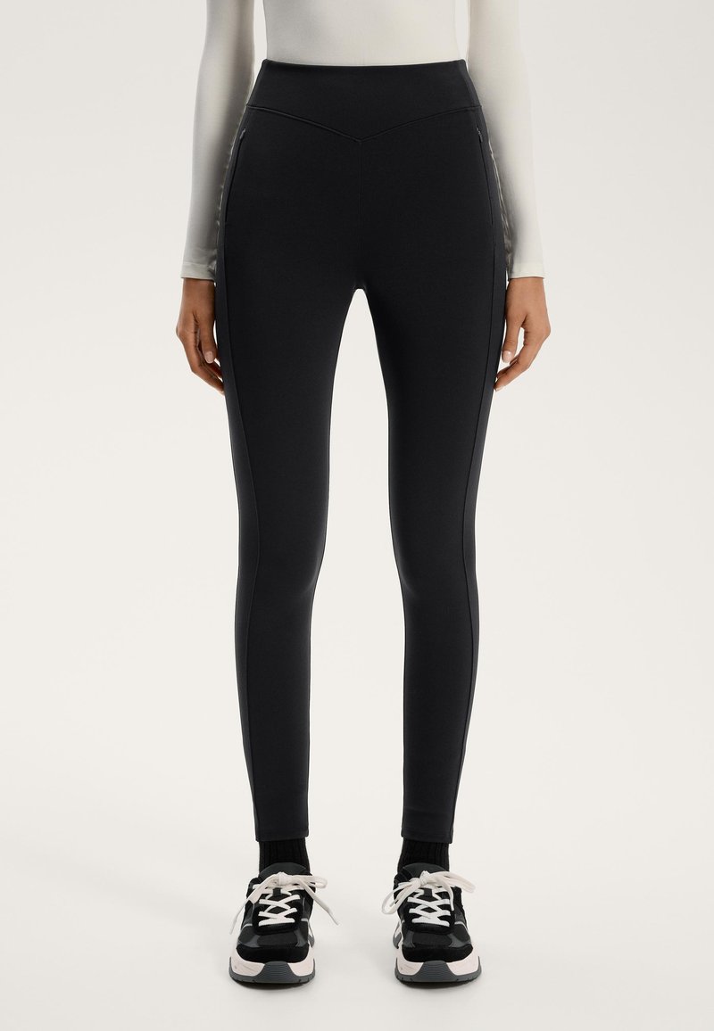 Zwarte leggings met hoge taille van een glad, rekbaar materiaal, voorzien van zijpanelen en een strak design, gecombineerd met zwart-witte sneakers.
