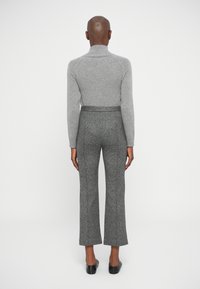 Siv turtleneck pulover, prilegajoča oblika in rebrasta tekstura. Razširjene, marmorirane sive hlače, srednji pas, mehak material. Črne slip-on čevlje zaokrožajo obleko.