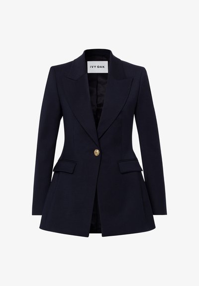 Blazer bleu marine cintré pour femme avec larges revers, fermeture par un bouton doré, poches à rabat et taille structurée de Ivy Oak.