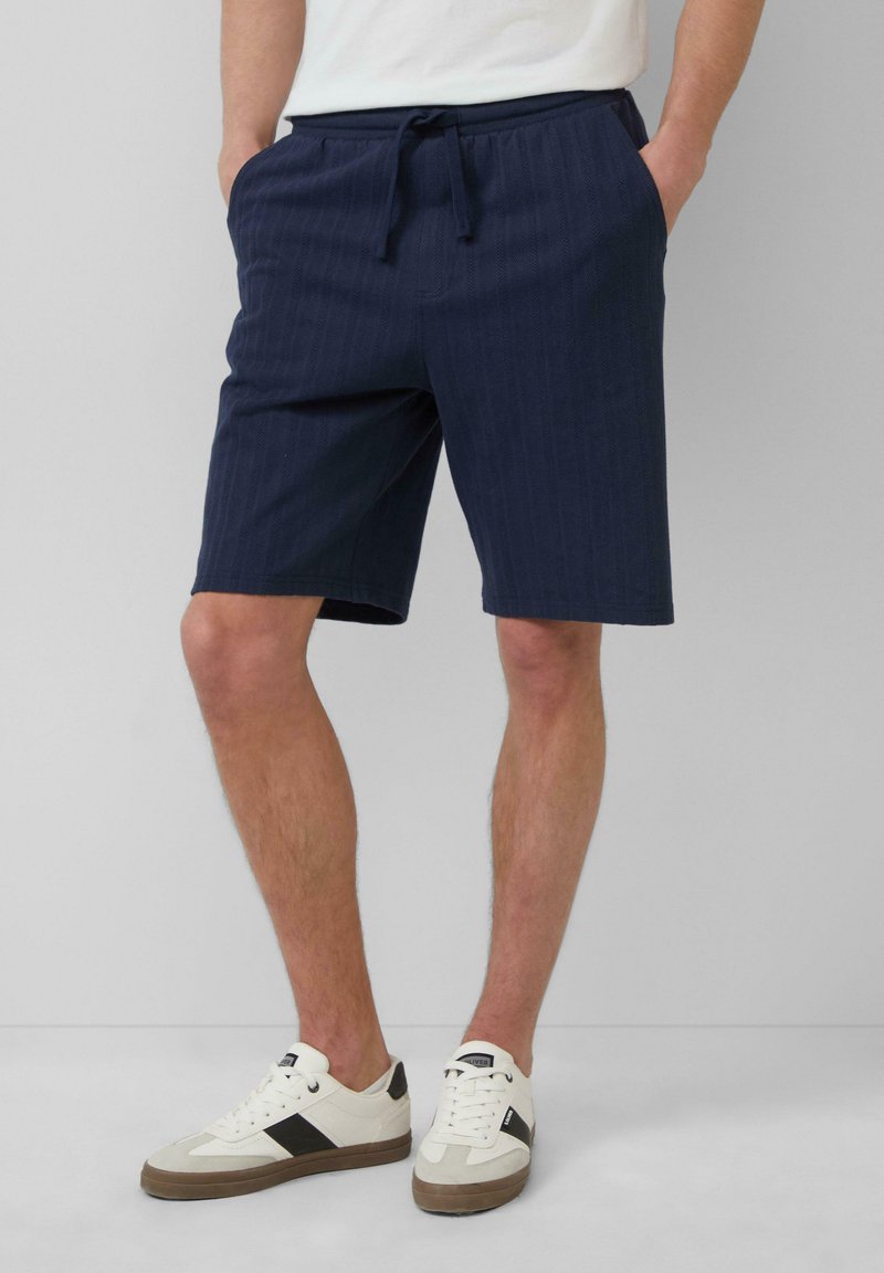 Shorts navy avec un motif de rayures verticales texturé, dotés d'une ceinture élastique avec cordon de serrage et de poches latérales.