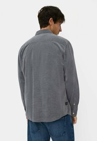 Graues Cordhemd mit Rückenteilen, Knopfmanschetten und abgerundetem Saum. Es zeichnet sich durch strukturierte Rippungen und ein kleines Logoschild an der unteren Seite aus.